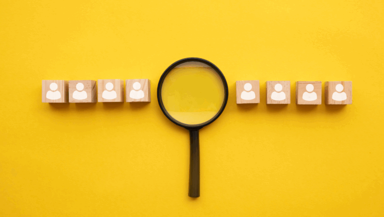 Representations of people on wooden blocks, with a magnifying glass, on yellow background.